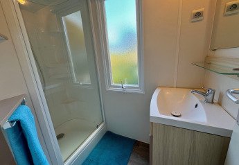 Bagno moderno in Comfort Cottage a Camping Le Périgord, con doccia, lavandino e grande finestra.