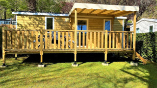 Cabane en bois Classic Cottage avec terrasse couverte, entourée de pelouse et d'arbres verdoyants.