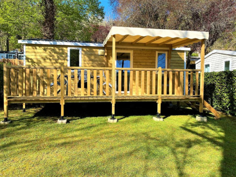 Casetta in legno Classic Cottage con veranda coperta, immersa nel verde tra alberi e prato curato.