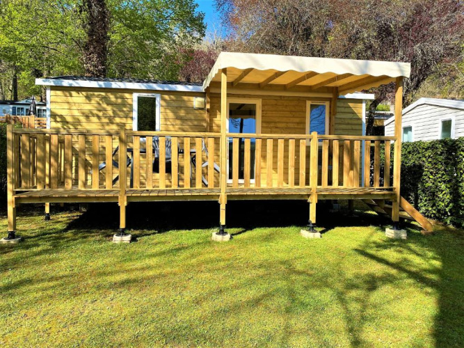 Cabaña Classic Cottage de madera con porche cubierto, rodeada de césped y árboles en la naturaleza.