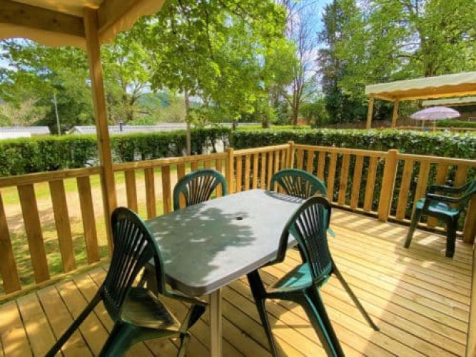 Terraza de madera exterior en Classic Cottage en Camping Le Périgord, Francia, con mesa y sillas plásticas.