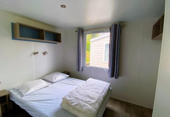 Soveværelse med dobbeltseng, vindue og enkel indretning i Classic Cottage på Camping Le Périgord i Frankrig.