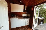Lille campingkøkken i træhus ved REBL Outdoor, Holland, med komfur, skabe og åben dør mod naturen.