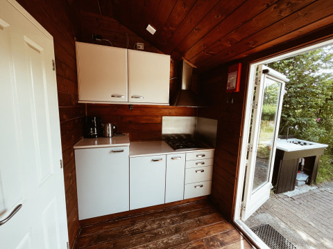 Cozy kitchen inside a wooden camping cottage at REBL Outdoor, Netherlands, with stove and open door.