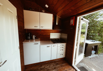 Piccola cucina in cottage di legno presso REBL Outdoor, Paesi Bassi, con fornelli e porta aperta sulla natura.