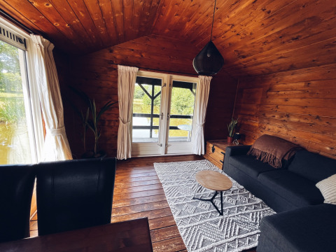 Accogliente cottage in legno presso REBL Outdoor Paesi Bassi, con divano, tappeto e vista stagno.