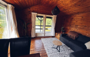 Acogedora cabaña de madera junto al estanque en REBL Outdoor, Países Bajos, con sofá y alfombra.