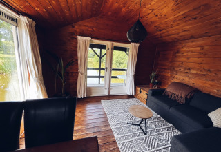Gezellige houten campinghut aan de vijver bij REBL Outdoor in Nederland, met zetel en zicht op het groen.