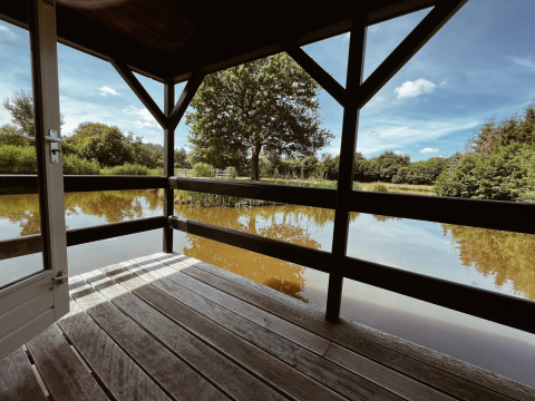 Udsigt fra en træterrasse ved en dam på REBL Outdoor, Camping cottage, omgivet af natur i Holland.