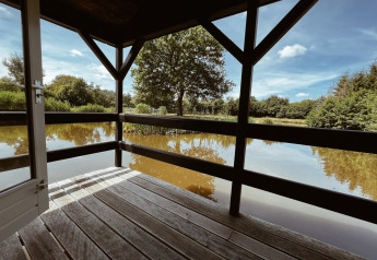 Vue depuis une terrasse en bois sur l’étang au Camping cottage de REBL Outdoor, entouré de nature hollandaise.