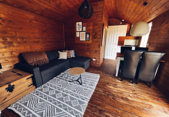 Interno di cottage da campeggio REBL Outdoor, Paesi Bassi, con pareti in legno, divano nero e zona pranzo.