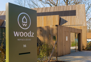 Toegang tot Woodz refined lodges, met een modern houten bord en gebouw omringd door natuur.
