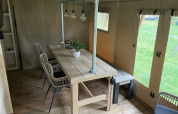 Dining area in a safari tent with wooden table, wicker chairs, and lights at Beerze Bulten, Netherlands.