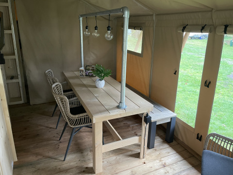 Coin repas sous tente safari avec table en bois, chaises en osier et lampes à Beerze Bulten, Pays-Bas.