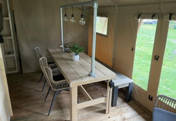 Comedor en tienda safari con mesa de madera, sillas de mimbre y luces en Beerze Bulten, Países Bajos.