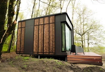 Nokken NKN-18 tiny house i træ og sort facade, placeret i skov omgivet af grønne træer i Wilsumer Berge, Tyskland.