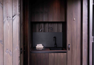 Pequeña cocina moderna de madera oscura y grifería negra en la Nokken NKN-18 Cabin en Wilsumer Berge, Alemania.