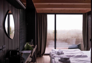Interior de la Nokken NKN-18 Cabin con grandes ventanales, cama y decoración moderna en Wilsumer Berge, Alemania.
