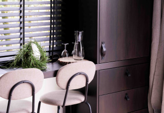 Interior moderno de casa pequeña con sillas, copas, detalles en madera y plantas junto a la ventana.