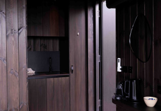 Interior de la Nokken NKN-18 Cabin en Wilsumer Berge, Alemania, con madera oscura y una pequeña cocina.
