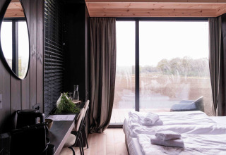 Casa diminuta moderna Nokken NKN-18 Cabin en Wilsumer Berge, Alemania, con ventana panorámica, cama y escritorio.