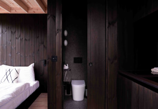 Interior moderno de la Nokken NKN-18 Cabin en Wilsumer Berge, Alemania, con madera oscura y cama.