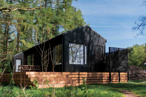 Schwarze Hütte namens Koya Tiny Cabin mit Holzterrasse im Waldgebiet Wilsumer Berge, Deutschland.