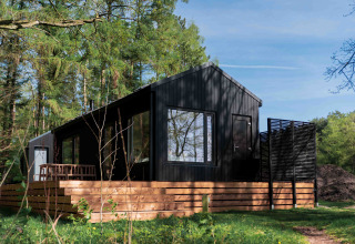 Schwarze Hütte namens Koya Tiny Cabin mit Holzterrasse im Waldgebiet Wilsumer Berge, Deutschland.