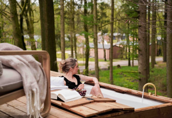 Mujer relajándose con vino en una bañera exterior en Koya Tiny Cabin, rodeada de bosque en Wilsumer Berge.