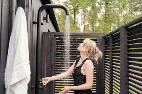 Vrouw geniet van een buitendouche bij Koya Tiny Cabin op Wilsumer Berge in Duitsland, omringd door donker hout