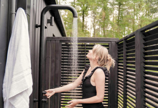 Vrouw geniet van een buitendouche bij Koya Tiny Cabin op Wilsumer Berge in Duitsland, omringd door donker hout