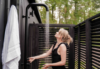 Mujer disfrutando de una ducha exterior en Koya Tiny Cabin en Wilsumer Berge, Alemania, rodeada de madera oscura