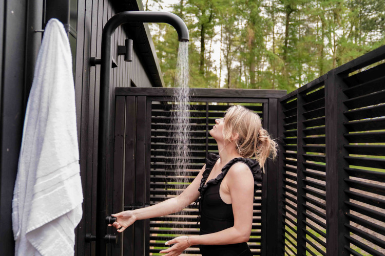 Woman enjoying an outdoor shower at Koya Tiny Cabin at Wilsumer Berge in Germany, surrounded by dark wood