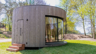Mini-maison ronde et moderne Lumni Pod avec façade en bois et grandes fenêtres dans un cadre verdoyant.