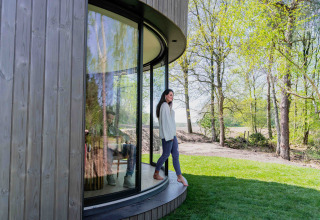 Una mujer está fuera de la tiny house Lumni Pod en Wilsumer Berge, Alemania, rodeada de verde y árboles.