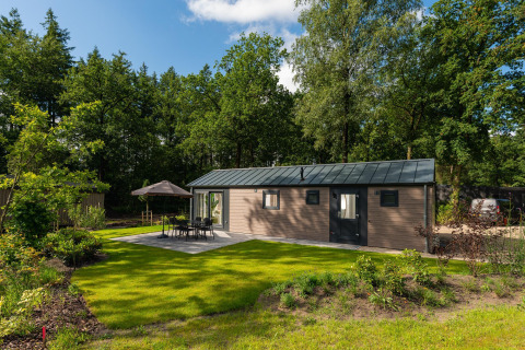 Lodge Velthorst Comfort con prato verde, tavolo da giardino, sedie e ombrellone, immerso nella natura.