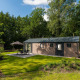 Lodge Velthorst Comfort con prato verde, tavolo da giardino, sedie e ombrellone, immerso nella natura.