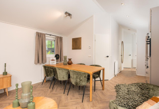 Dining area with a wooden table and green chairs in a modern lodge at Velthorst Comfort, Veluwepark de Bosgraaf, Netherlands.