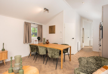 Comedor con mesa de madera y sillas verdes en un lodge moderno en Velthorst Comfort, Veluwepark de Bosgraaf, Países Bajos.