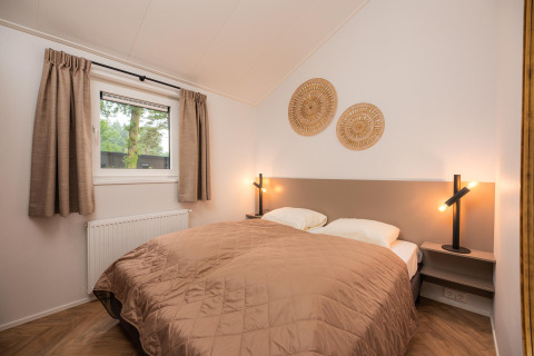 Bedroom with double bed, beige quilt, modern lamps and woven wall art at Velthorst Comfort, Veluwepark de Bosgraaf.
