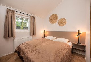 Bedroom with double bed, beige quilt, modern lamps and woven wall art at Velthorst Comfort, Veluwepark de Bosgraaf.