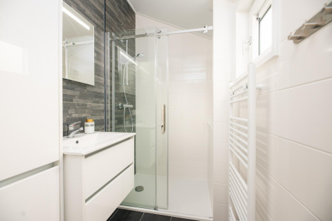 Modern bathroom with glass shower, white vanity, and dark tiled wall at Velthorst Comfort in the Netherlands.
