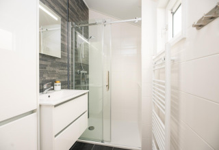 Modern bathroom with glass shower, white vanity, and dark tiled wall at Velthorst Comfort in the Netherlands.