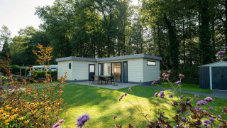 Außenansicht des Comfort Chalet, umgeben von grünem Rasen, Blumen und einem bewaldeten Hintergrund.