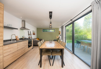 Moderne spise- og opholdsområde i Comfort Chalet ved Veluwepark de Bosgraaf, Holland, med store vinduer.