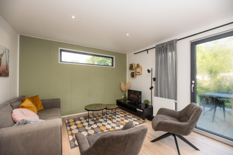 Sala moderna en Comfort Chalet de Veluwepark de Bosgraaf, Países Bajos, con sofá, sillones y televisor.