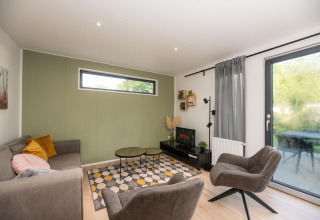 Sala moderna en Comfort Chalet de Veluwepark de Bosgraaf, Países Bajos, con sofá, sillones y televisor.