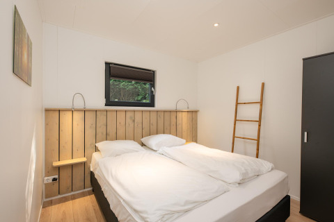 Dormitorio con cama doble, suelo de madera y escalera en Comfort Chalet de Veluwepark de Bosgraaf, Países Bajos.