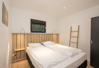Dormitorio con cama doble, suelo de madera y escalera en Comfort Chalet de Veluwepark de Bosgraaf, Países Bajos.