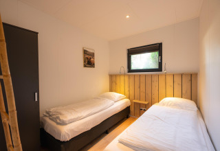 Zimmer mit zwei Einzelbetten, Fenster und Schrank im Comfort Chalet im Veluwepark de Bosgraaf, Niederlande.